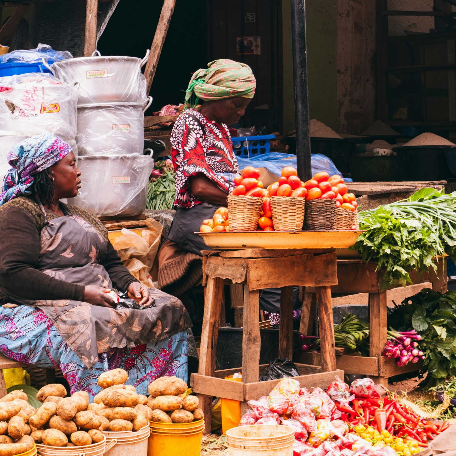 Two women selling vegetables at a market stall with baskets of produce.