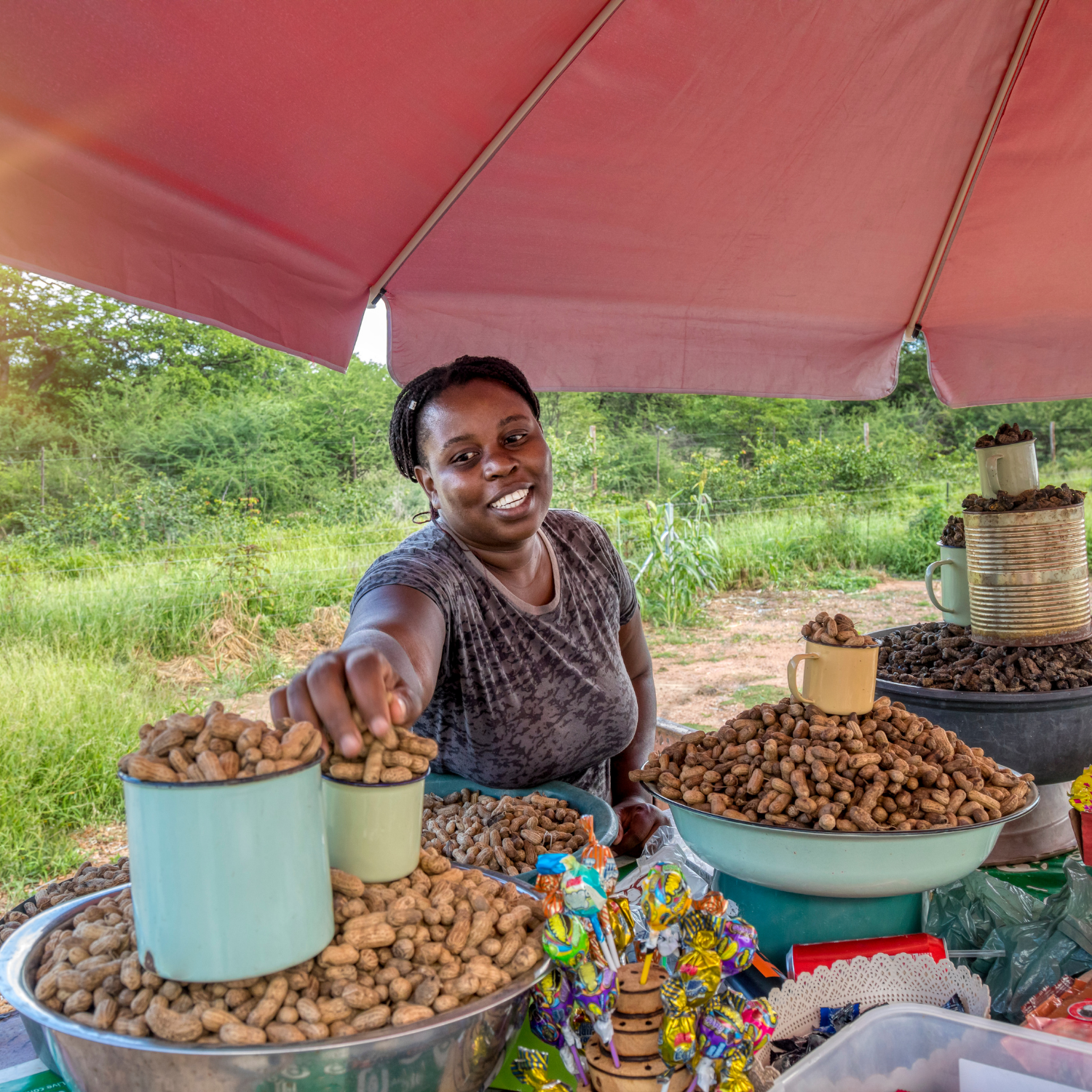 Woman selling farm produce under a pink canopy in an outdoor setting