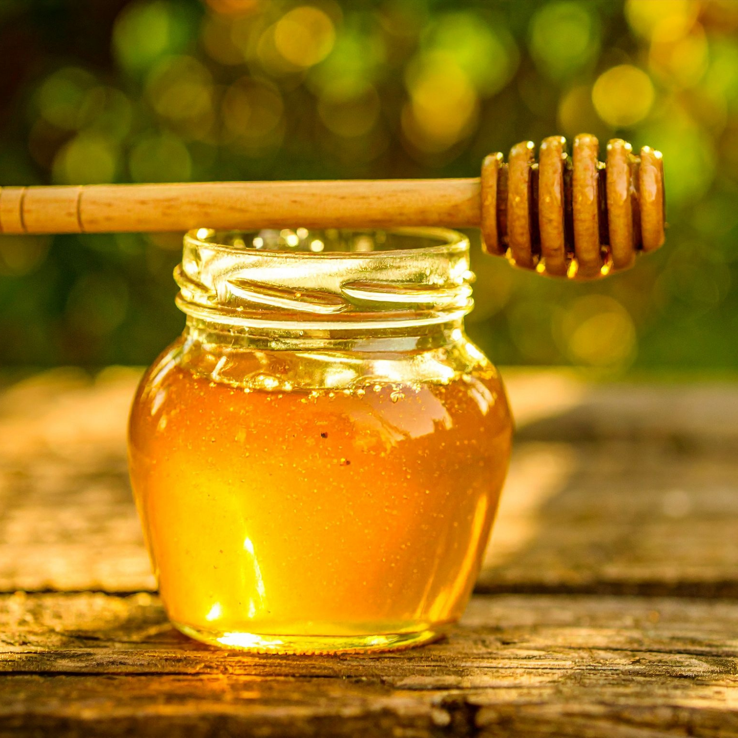 Jar of honey with a wooden dipper on a wooden surface with a blurred natural background