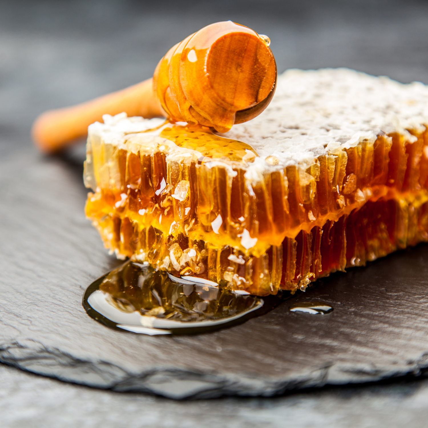 Close-up of golden honeycomb with honey dripping on a dark surface — showcasing Joreen Brands natural unfiltered wild honey in its pure form.